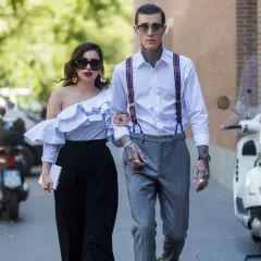 Pareja elegante pasea, él es un invitado boda hombre sin traje, con tirantes y tatuajes. Ella lleva un top blanco voluminoso.