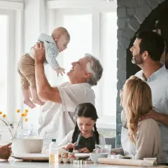 Radosna rodzina w kuchni. Dziadek podrzuca wnuka, babcia patrzy z uśmiechem. Dzieci pieką ciasteczka. To są prawdziwe babciowe dla kogo!