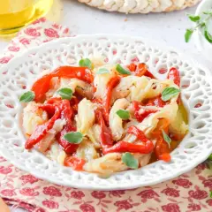 Deliciosa ensalada de bacalao con pimientos rojos asados y hierbas frescas, servida en un plato blanco decorado.