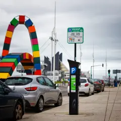 Panneaux de stationnement payant et horodateur, rappelant qu'une amende stationnement non payé est possible. Au loin, une arche colorée.