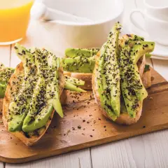 Tostadas con aguacate y semillas negras, perfectas para desayunos veganos. Acompañadas de zumo de naranja y limón.
