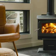 Un confortable fauteuil en cuir brun fait face à un poêle à bois non étanche, où des flammes dansent joyeusement dans le foyer.