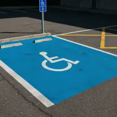 Niebieskie miejsce parkingowe dla niepełnosprawnych, oznaczone symbolem wózka, jest częścią wspólnoty dbającej o dostępność.