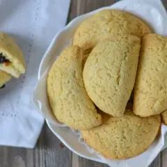 Dolci tipici bologna: biscotti dorati ripieni di marmellata, serviti in una ciotola bianca su un tovagliolo.