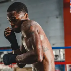 A boxer, sweat glistening, prepares for a head punch in the ring.