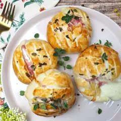 Quattro fagottini dorati con prosciutto e **tomino fuso** che cola, guarniti con erbe aromatiche su un piatto rosa.