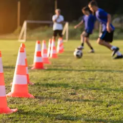 Trening piłkarski z użyciem pachołków, pokazujący jak uczyć futbolu. Dzieci ćwiczą drybling na boisku.