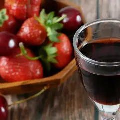 Szklanka ciemnego płynu, prawdopodobnie ratafia wódka, obok miski pełnej świeżych truskawek i wiśni.