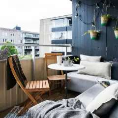 Mysig, inredd långsmal balkong med soffa, bord, stolar och hängande amplar. Perfekt för avkoppling.