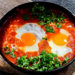 Herzhaftes Shakshuka-Rezept: Eier in würziger Tomatensoße, garniert mit frischer Petersilie, serviert in einer Gusseisenpfanne.