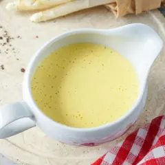 Cremige Sauce Hollandaise in einer Sauciere, daneben Spargel und Zitronenspalte. Perfekt für ein Frühlingsgericht.