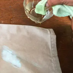 Mani che tamponano una macchia di vernice secca su un tessuto beige con un panno umido, per togliere macchie di vernice secca dai vestiti.