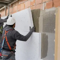Operai in cantiere applicano pannelli per l'isolamento esterno di un edificio, migliorando l'efficienza energetica.