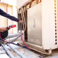 Técnico realiza soldadura con nitrógeno en unidad de aire acondicionado exterior, conectando manómetros a tuberías.