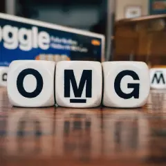 Dadi con lettere formano l'acronimo in inglese "OMG". Sullo sfondo, la scatola del gioco Boggle.