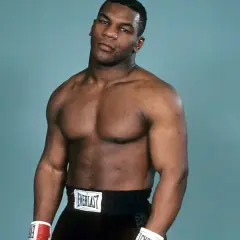Mike Tyson's powerful physique is on full display, showcasing his legendary mike tyson abs and muscular chest. He wears boxing shorts and gloves.