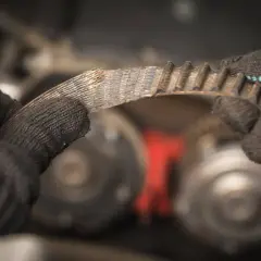 Zużyty, piszczący pasek klinowy w rękach mechanika. Widać postrzępione krawędzie i zużycie.