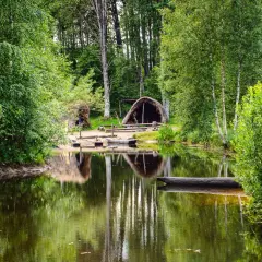 En stilla sjö speglar grönskande träd och en hydda vid Årås kvarn. En stockbåt vilar vid strandkanten.