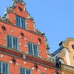 Fasaderna på ett gammalt hus i Stockholm, som en gång kan ha varit ett slott eller värdshus, med detaljerad utsmyckning och röda och gula färger mot en blå himmel.