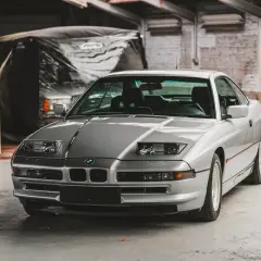 Un elegante BMW E31 plateado, un clásico deportivo, descansa en un garaje con paredes de ladrillo.