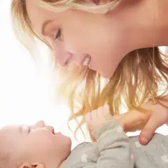 Uśmiechnięta mama pochyla się nad dzieckiem, które ma czkawkę u noworodka.