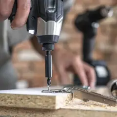 Instrucciones sobre como poner una broca en un taladro. Un hombre usa un taladro para fijar una bisagra a un tablero de madera.