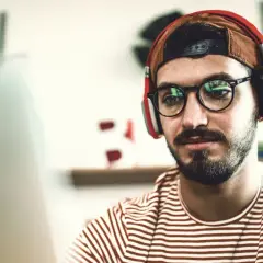 Junger Mann mit Kopfhörern und Brille lernt für seinen berufsbegleitenden Master in Stuttgart.