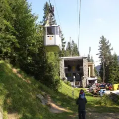 Kolejka linowa PKL wjeżdża na stację w Kuźnicach. W tle góry i las.