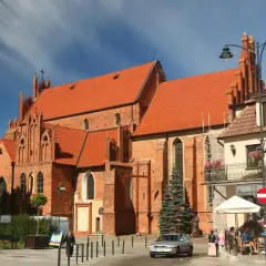 Starogard Gdański atrakcje: ceglana bazylika z czerwonym dachem i gotyckimi detalami, plac z kawiarnią i ludźmi.