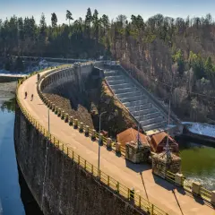 Spacerowicze na trasie zapory Pilchowice. Majestatyczna konstrukcja z kamienia i betonu otoczona lasem.