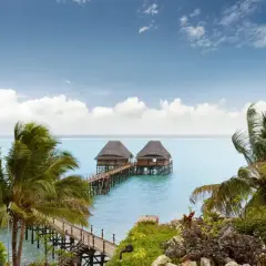 Dwa domki na wodzie na Zanzibarze, otoczone palmami. Nawet podczas pory deszczowej Zanzibar zachwyca pięknem.