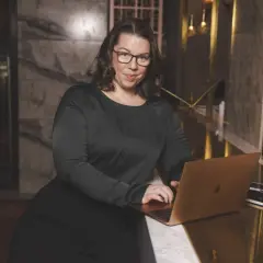 Linnea Molander, med glasögon och svart klänning, arbetar vid en bärbar dator i en lyxig miljö.