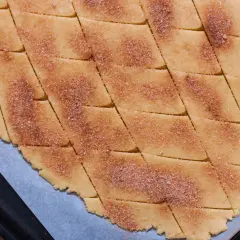 Surowe ciasto na ciasteczka pokrojone w romby, posypane cukrem z cynamonem.