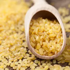 Kasza bulgur na drewnianej łyżce. Niska zawartość błonnika wpływa na jej indeks glikemiczny.