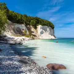 Weiße Kreidefelsen ragen steil auf, bewaldet von oben. Die Ostsee bei Sassnitz schimmert türkisblau, ein Kiesstrand lädt zum Verweilen ein.