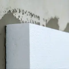Biały styropian przyłożony do ściany z zaprawą. Czy to styrobeton czy styropian? Izolacja budynku.