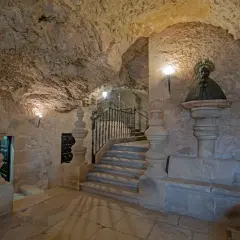 Busto de San Saturio en Soria, junto a escaleras de piedra y rejas, en un entorno rocoso.