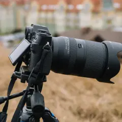 Aparat fotograficzny z obiektywem 18-300mm na statywie, z rozmytym budynkiem w tle.