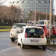 Biały Volkswagen i inne samochody stojące na ulicy, typowe parkowanie w Wiedniu.