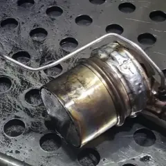 Metalowy element układu wydechowego z widocznymi śladami zużycia i zabrudzeń.