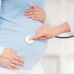 Lekarz osłuchuje brzuch ciężarnej, sprawdzając, czy nie ma ułożenia poprzecznego, które mogłoby wymagać cesarki.