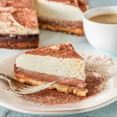 Pyszna tarta z mascarpone i czekoladą, posypana kakao, czeka na widelczyk. Obok filiżanka kawy.