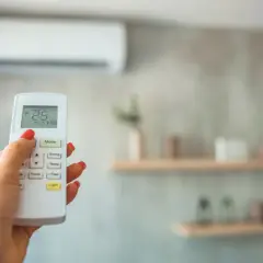 Mano con mando a distancia de aire acondicionado, ajustando la temperatura. Ideal para calcular potencia aire acondicionado y optimizar el confort.