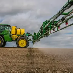 Zielony opryskiwacz rolniczy z żółtym zbiornikiem opryskuje pole.