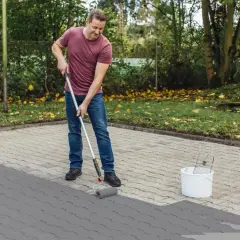 Mężczyzna maluje betonowy chodnik na szaro wałkiem.