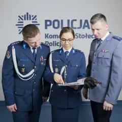 Policjanci w mundurach omawiają materiały. Pokazują, jak nosić furażerkę policja.