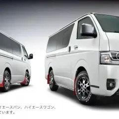 Dwa białe vany Toyota Hiace z pakietem GR Parts, jeden z tyłu, drugi z przodu, z czerwonymi błotnikami.