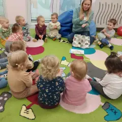 Nauczycielka pokazuje dzieciom w żłobku obrazki, inspirując angielski w żłobku pomysły. Dzieci siedzą na kolorowym dywanie.