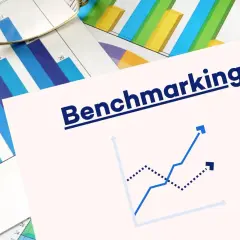 Okulary na wykresach słupkowych i liniowych. Na pierwszym planie napis "Benchmarking" i dwa wykresy liniowe, jeden rosnący, drugi malejący.