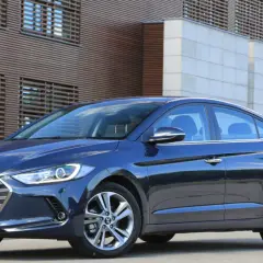 Ciemnoniebieski Hyundai Elantra 2023 zaparkowany przed nowoczesnym budynkiem z drewnianą fasadą.